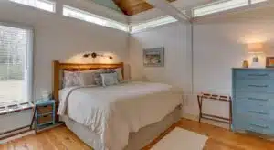 Bedroom with white walls, white trim, hardwood flooring, wooden headboard, and blue dresser