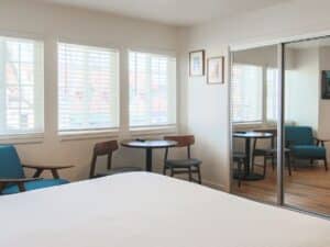 Bedroom with bed, mirrored closet doors, table and three chairs, TV over buffet table and three windows