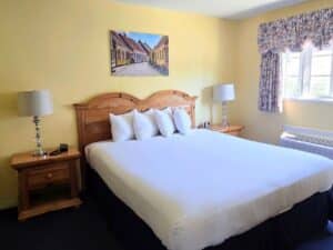 Bedroom with queen bed in white sheets, large window with floral valence, side tables with lamps