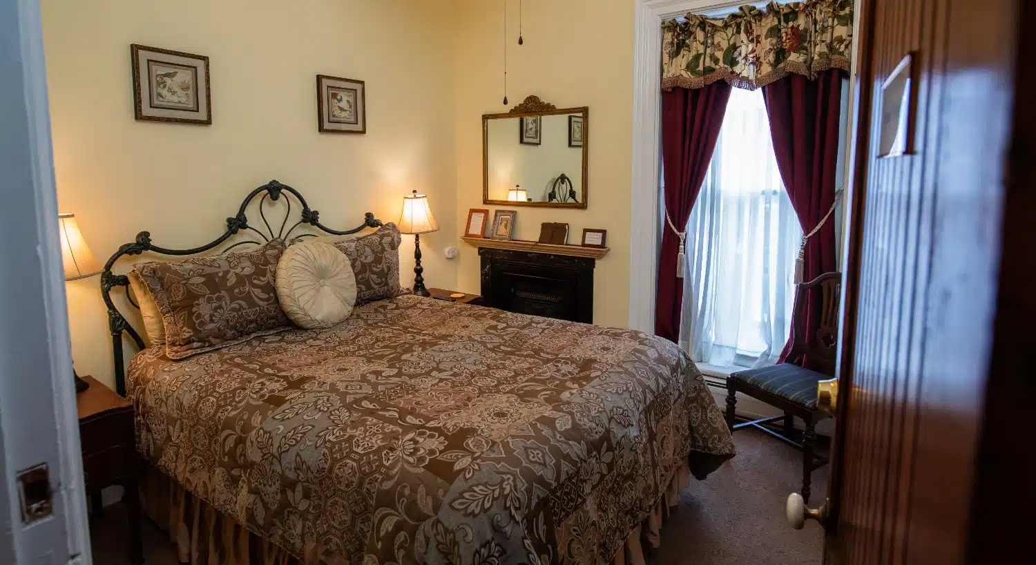 Bedroom with light yellow walls, white trim, wrought iron bed with multicolored bedding, fireplace, and large window