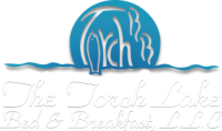 Logo for The Torch Lake Bed & Breakfast, LLC. Features a stylized blue sun or moon over water, highlighting the charm of Torch Lake, with "Torch" and cursive white text reading "The Torch Lake Bed & Breakfast L.L.C.